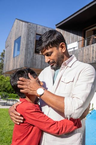 Asian father and son embracing on sunny lawn bonding affection