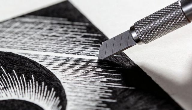 Macro linocut carving with precision craft knife blade creating cross-hatch texture