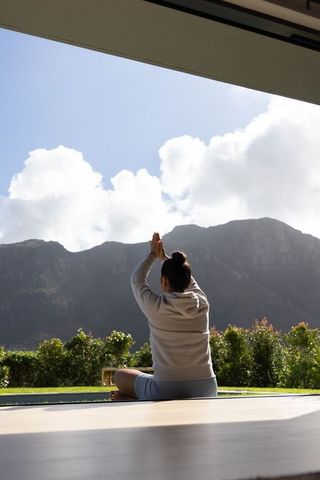 Woman practicing sunrise yoga on veranda facing dramatic mountain range and cloudscape