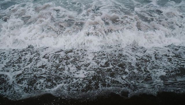 Stormy ocean waves crashing, forming lacy white foam patterns on dark wet sand at coastal shore