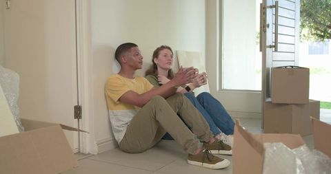 Young couple unpacking new home taking coffee break sitting on tiled floor in sunlight