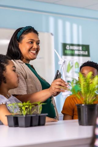 Asian educator teaching renewable energy with wind turbine model and seedlings in classroom
