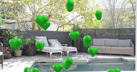 Green heart balloons floating over backyard pool patio with white chaise lounges