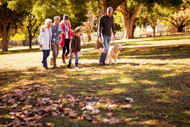 Multigenerational family enjoying a walk with their dog in a park during autumn. Ideal for promoting family activities, outdoor leisure, pet-friendly environments, and intergenerational bonding. Suitable for use in advertisements, brochures, and websites related to family, pets, and outdoor recreation.