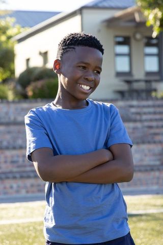 African american boy standing with crossed arms smiling in blue t-shirt outdoors