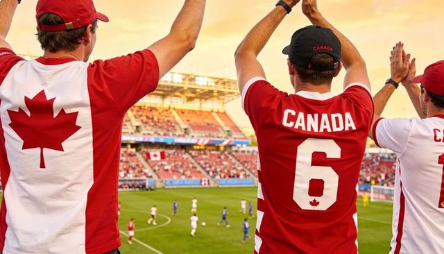 Canadian soccer fans cheering in stadium wearing red canada jerseys and caps at golden hour