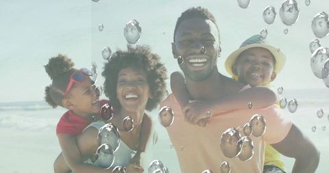 Happy family enjoying beach with parents carrying children on shoulders