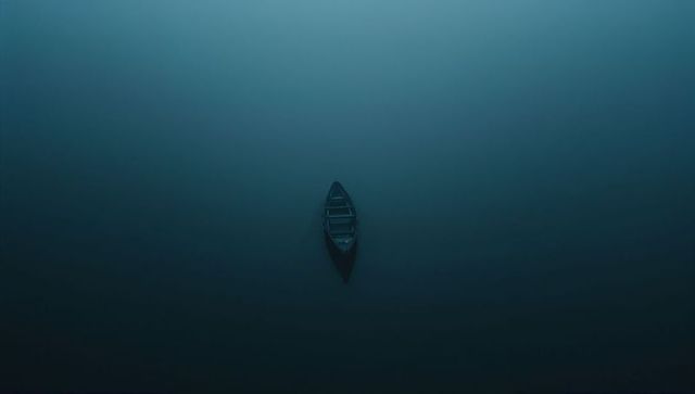 Solitary wooden rowboat drifting over misty lake minimal aerial silhouette