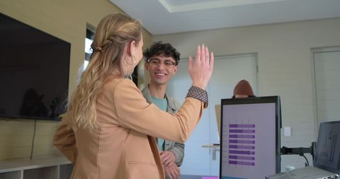 Team collaborating in modern workspace giving high five beside purple bar chart on monitor
