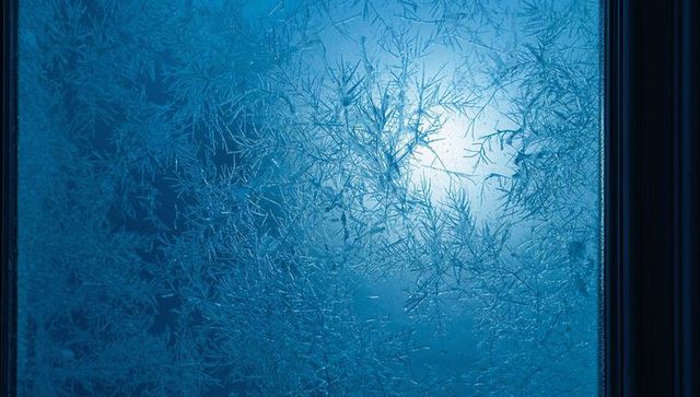 Frosted window panel revealing intricate ice crystal patterns with blue backlight glow