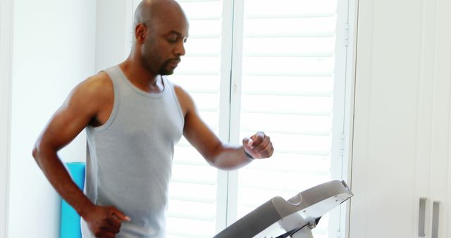 An African American man is checking his fitness tracker while walking on a treadmill, with copy space. His focus on health and technology illustrates the modern approach to personal wellness and exercise.