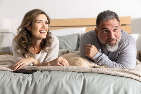 Middle-aged couple relaxing on bed with sleeping golden retriever, cozy morning comfort