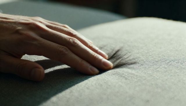 Hand pressing tufted cushion closeup showing woven fabric texture and gentle touch comfort