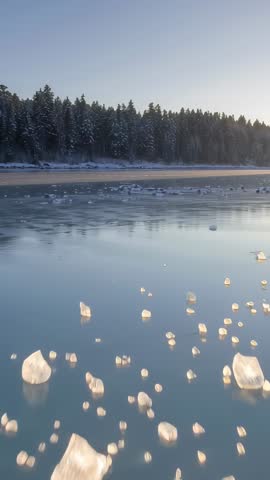 Vertical sunrise lifting and panning over icy lake with floating ice shards and snowy pines