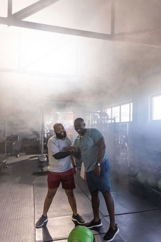 Two african men training together in bright gym fist bump after strength workout