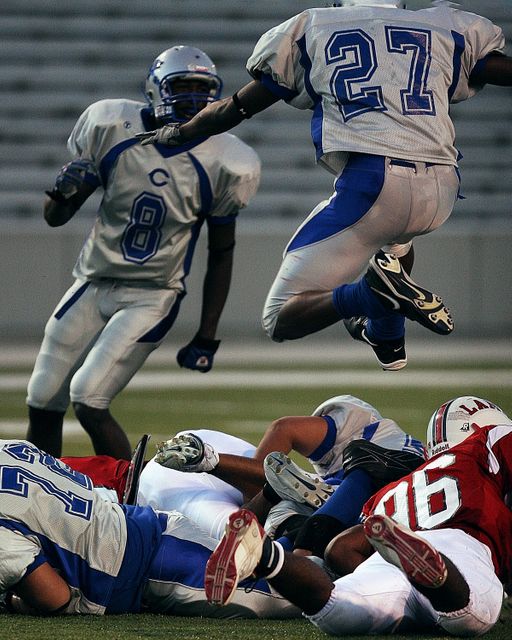 Football players wearing blue and white uniforms engage in competitive game action on field, showcasing intense athleticism and teamwork. Possible usage includes sports event promotions, athleticwear advertisements, sports blogs, and educational materials on football.