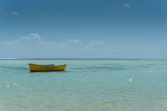 Yellow boat floating on clear ocean water under blue sky. Useful for themes of solitude, tranquility, summer vacations, and tropical destinations. Ideal for travel brochures, beach resorts, and relaxation concepts.
