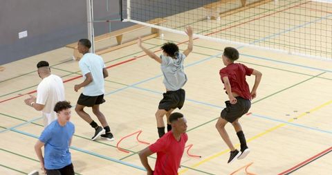 Multiethnic male volleyball team training jumping over red hurdles near net indoor court