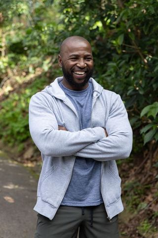 African american man smiling with arms crossed standing on forest trail casual outdoor
