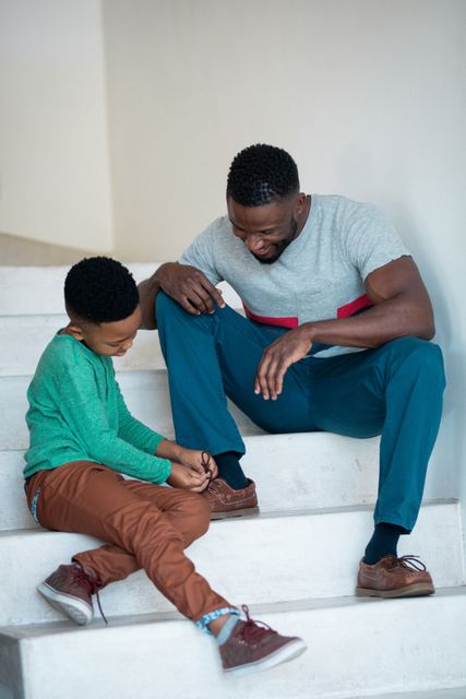 African american son tying shoes to his father on stairs. family life, spending time together at home.