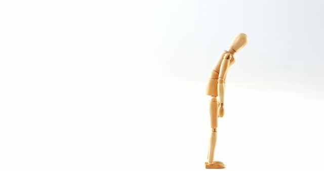 A wooden artist's mannequin is posed in a bowing gesture, with copy space. Its simple form and the plain background offer a minimalist aesthetic that can symbolize humility or performance.