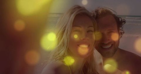 Smiling couple taking beach selfie at sunset with golden bokeh and backlit glow