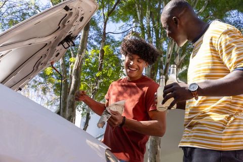 Friends checking oil on car while sharing drinks outdoors