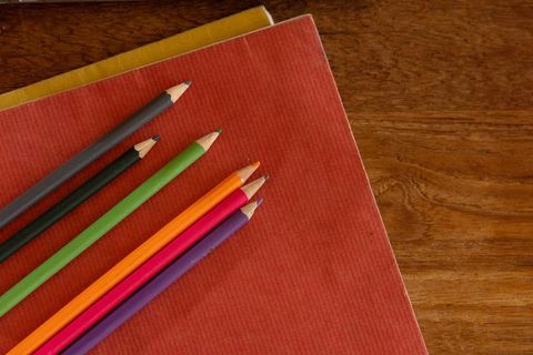 Colorful Pencils Resting on Red Notebook on Wooden Desk with Generous Copy Space