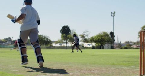 Batsman running between wickets wearing helmet and pads on sunny cricket field