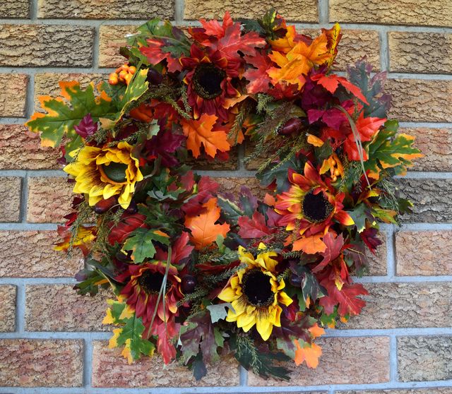 Autumn wreath featuring sunflowers and colorful leaves hanging on a brick wall. Perfect for seasonal decorating ideas, nature-inspired designs, or cozy home adornments. Ideal for use in home decor magazines, DIY project guides, and festive advertisement campaigns.