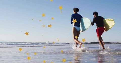 Wading couple carrying shortboards into shallow surf under clear sky with gold stars