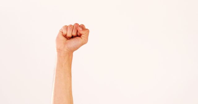 A raised fist of a Caucasian person against a plain background, with copy space. It symbolizes strength, unity, or resistance and is often associated with movements for social change.