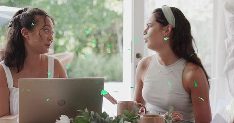 Two Women Collaborating Over Laptop and Coffee in Sunlit Home With Greenery