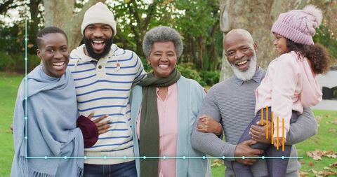 Multigenerational Family Smiling Together in Autumn Park Wearing Knit Beanies and Scarves