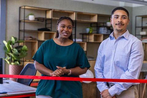 Diverse colleagues cutting red ribbon at modern office ceremony