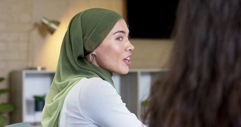 Woman wearing olive green hijab leading collaborative office discussion with colleagues