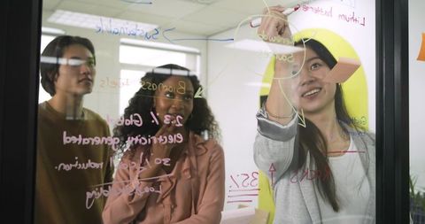 Diverse professionals collaborating on glass whiteboard in modern office