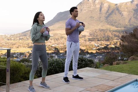 Active workout partners exercising with kettlebells poolside