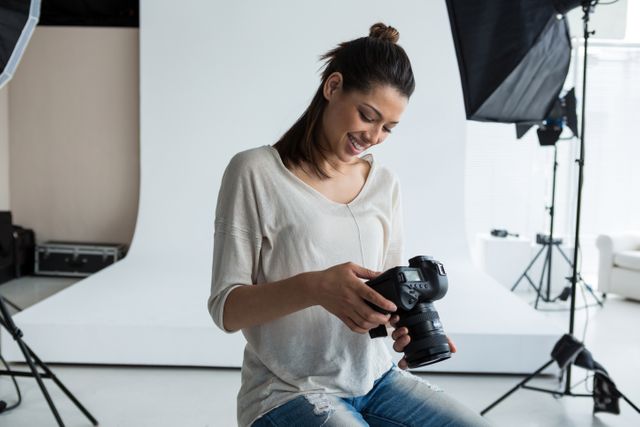 Female photographer reviewing captured photos on a digital camera in a bright studio. Ideal for content related to professional photography, camera equipment, photo shoots, and behind-the-scenes in photography studios.