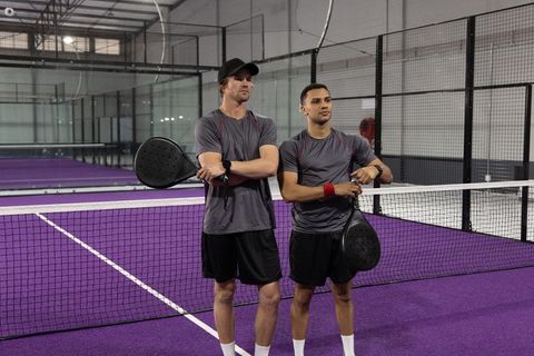 Male padel doubles team posing at net on purple indoor court for training and competition