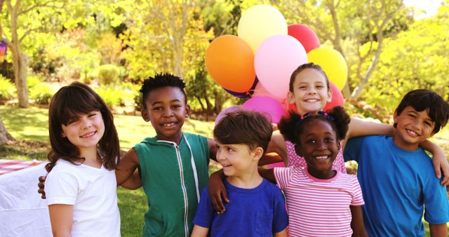 Perfect for advertisements, websites, or brochures promoting outdoor activities, children’s parties, or summer events. A diverse group of young children smiling, holding balloons, and enjoying an outdoor celebration in a park.