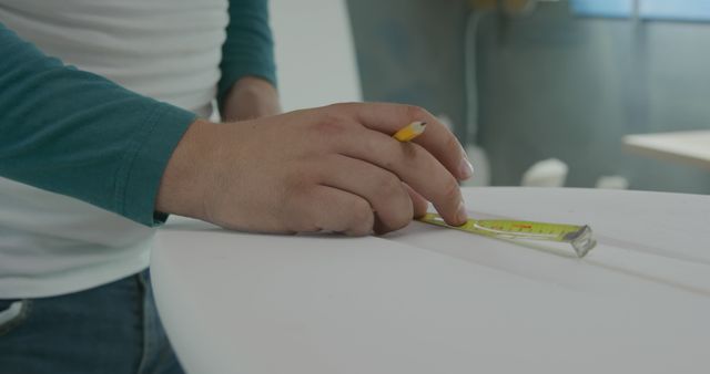 Hands measuring wooden or fabric piece using tape measure in workshop. Useful for topics on DIY projects, precise measurements, woodworking, crafting, and handwork activities.