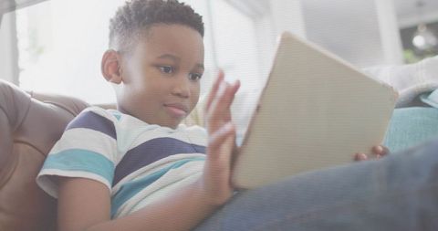 Reclining African American Boy Using Tablet on Couch for Relaxed Home Learning and Play