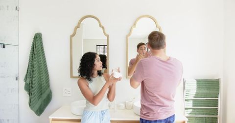 Couple sharing skincare routine in modern bathroom with gold-framed mirrors