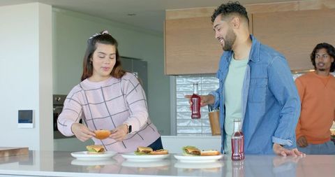 Friends assembling burgers at modern kitchen island sharing drinks and laughter