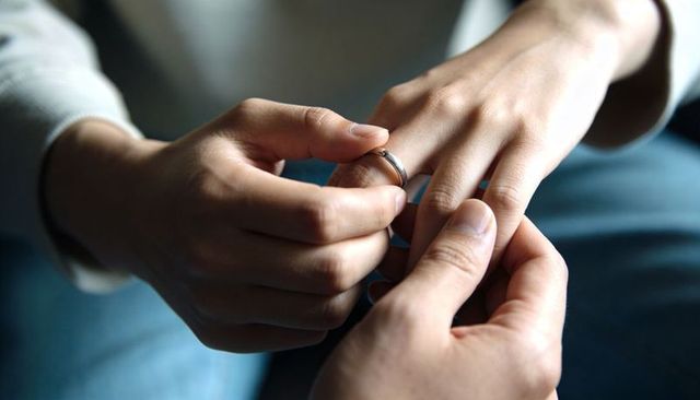 Sliding wedding band onto finger closeup conveying intimacy, commitment and tender moment