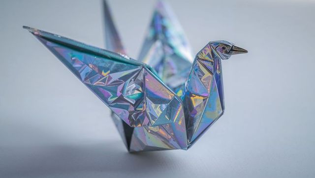 Shimmering Holographic Origami Crane Showing Iridescent Faceted Folds on Pale Tabletop