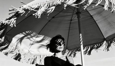 Monochrome portrait of woman sitting under fringed parasol casting bold shadow patterns