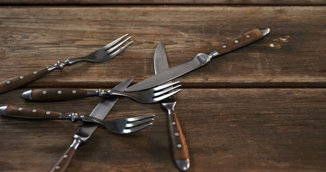 Forks and knives are arranged in a hashtag pattern on a rustic wooden table, with copy space. This creative display of cutlery adds a touch of whimsy to the dining setup.