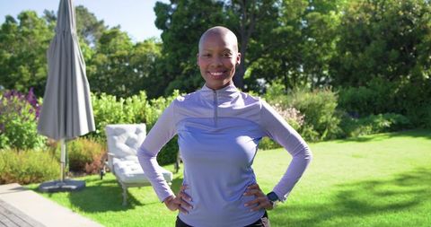 Bald african american woman smiling and posing in backyard garden wearing purple top